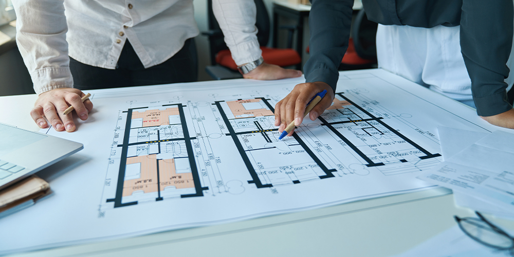 Two professionals reviewing architectural floor plans and system layouts for an underfloor heating project in a design office.